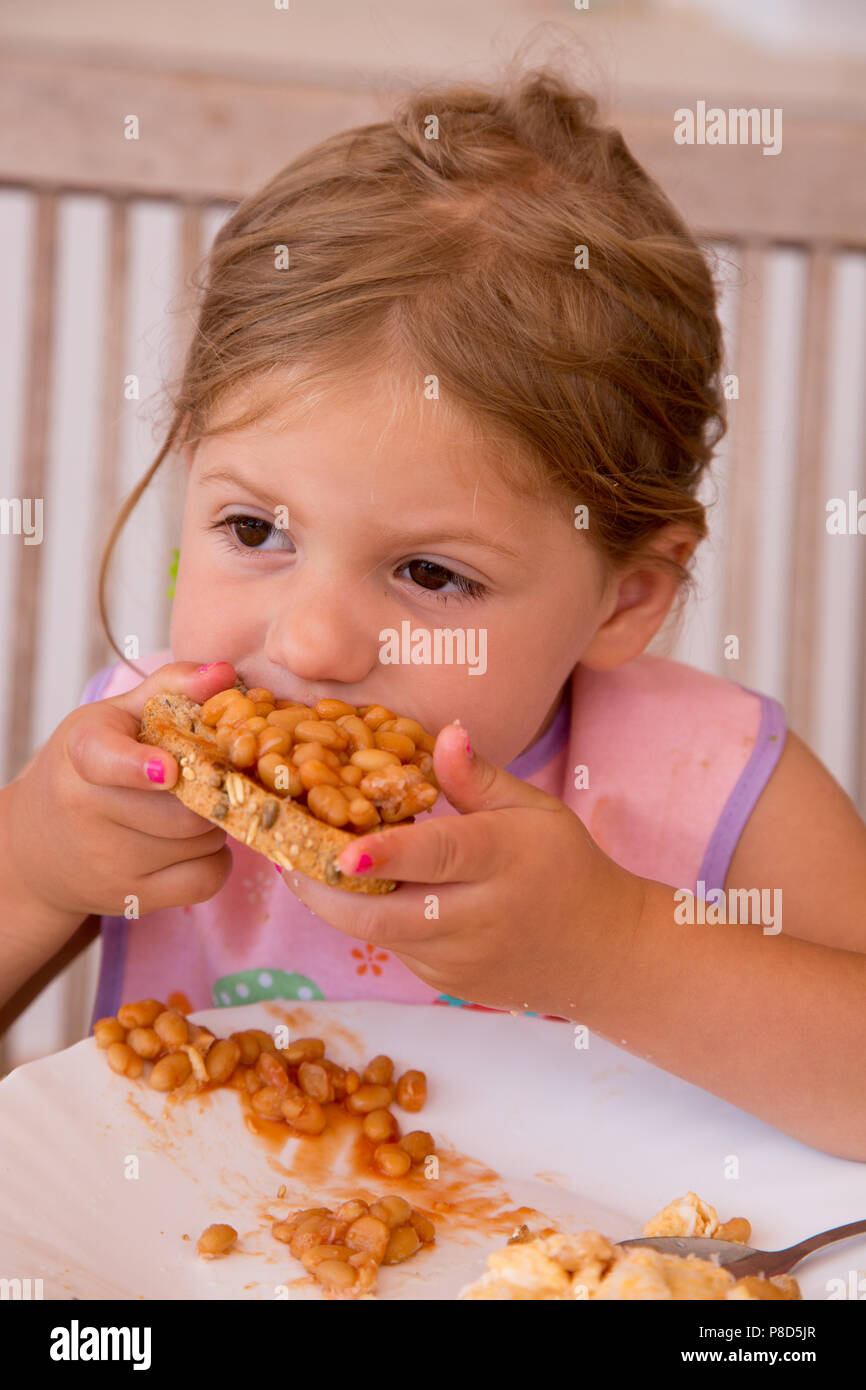 Ein Mädchen von zwei Einhalb Essen gebackene Bohnen auf Toast mit Rührei Stockfoto
