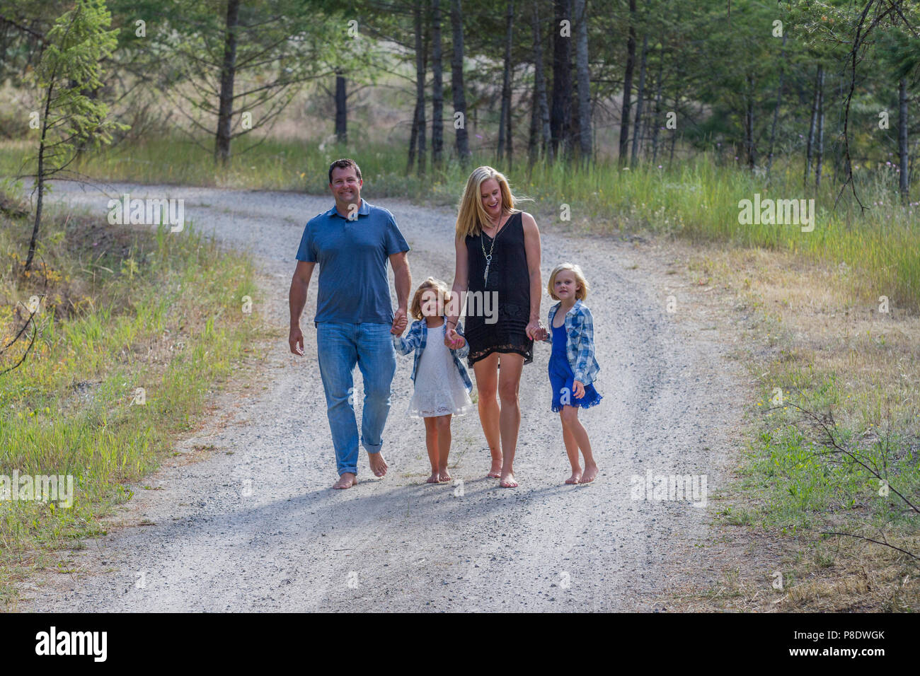 Attraktiver Mann und Frau, mit ihren 4 und 6 Jahre alten Töchter, wandern nach unten ein Land Feldweg, halten sich an den Händen, barfuß. Model Released - Vati Nr. 116, Gi Stockfoto