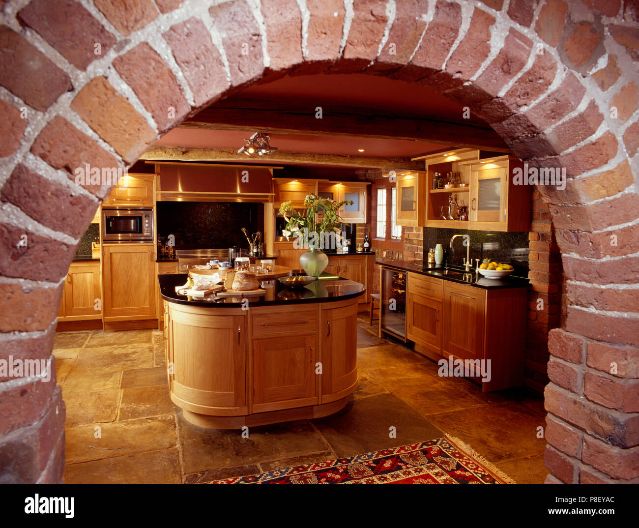 Blick durch gemauerte Bogen von traditioneller Küche aus Holz mit ovalen Insel- und Steinböden Stockfoto
