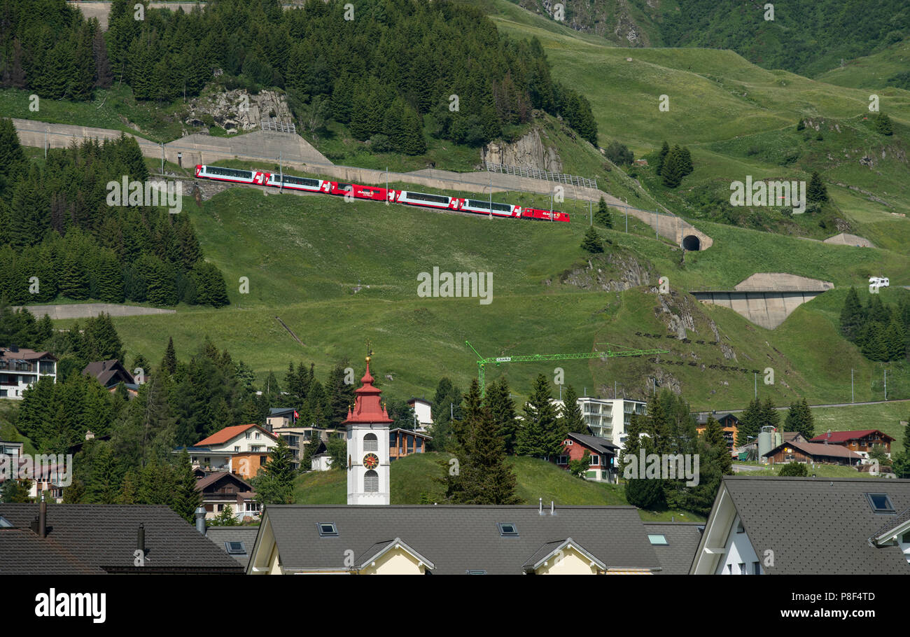 Andermatt im Kanton Uri, Schweiz, an denen Schweizer Berg Trains-Glacier Express - klettern hinauf Richtung Oberalppass und schweizer Fahnen. Juni 2018 Stockfoto