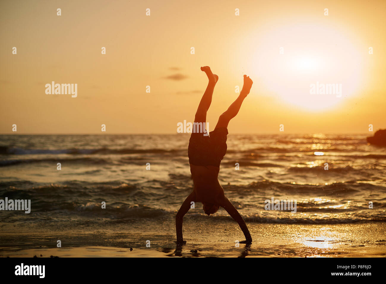 Junge in einer ungewöhnlichen sportlichen Pose am Meer bei Sonnenuntergang Stockfoto