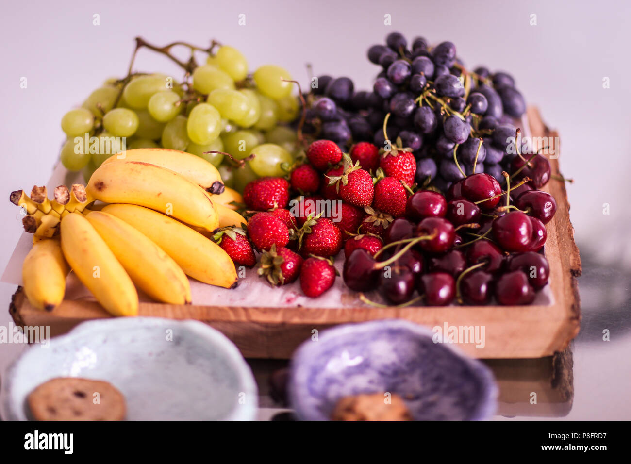 Früchte (weiße und blaue Trauben, Bananen, Erdbeeren und Kirschen) auf einer Holzplatte Stockfoto