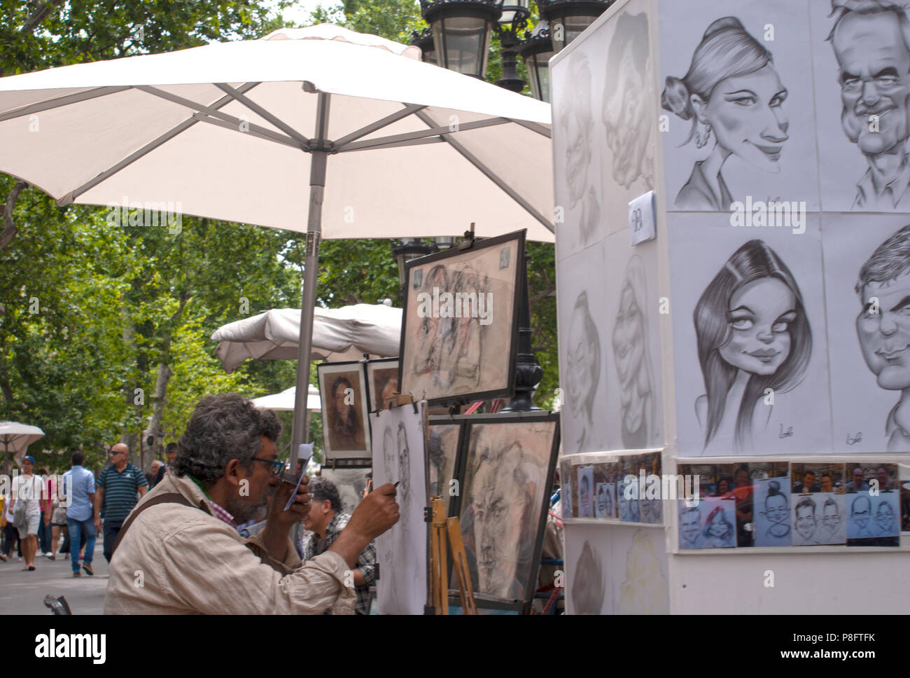 Ein street artist unter einem Sonnenschirm Zeichnung eine Karikatur Las Ramblas Barcelona Spanien Europa sitzen Stockfoto