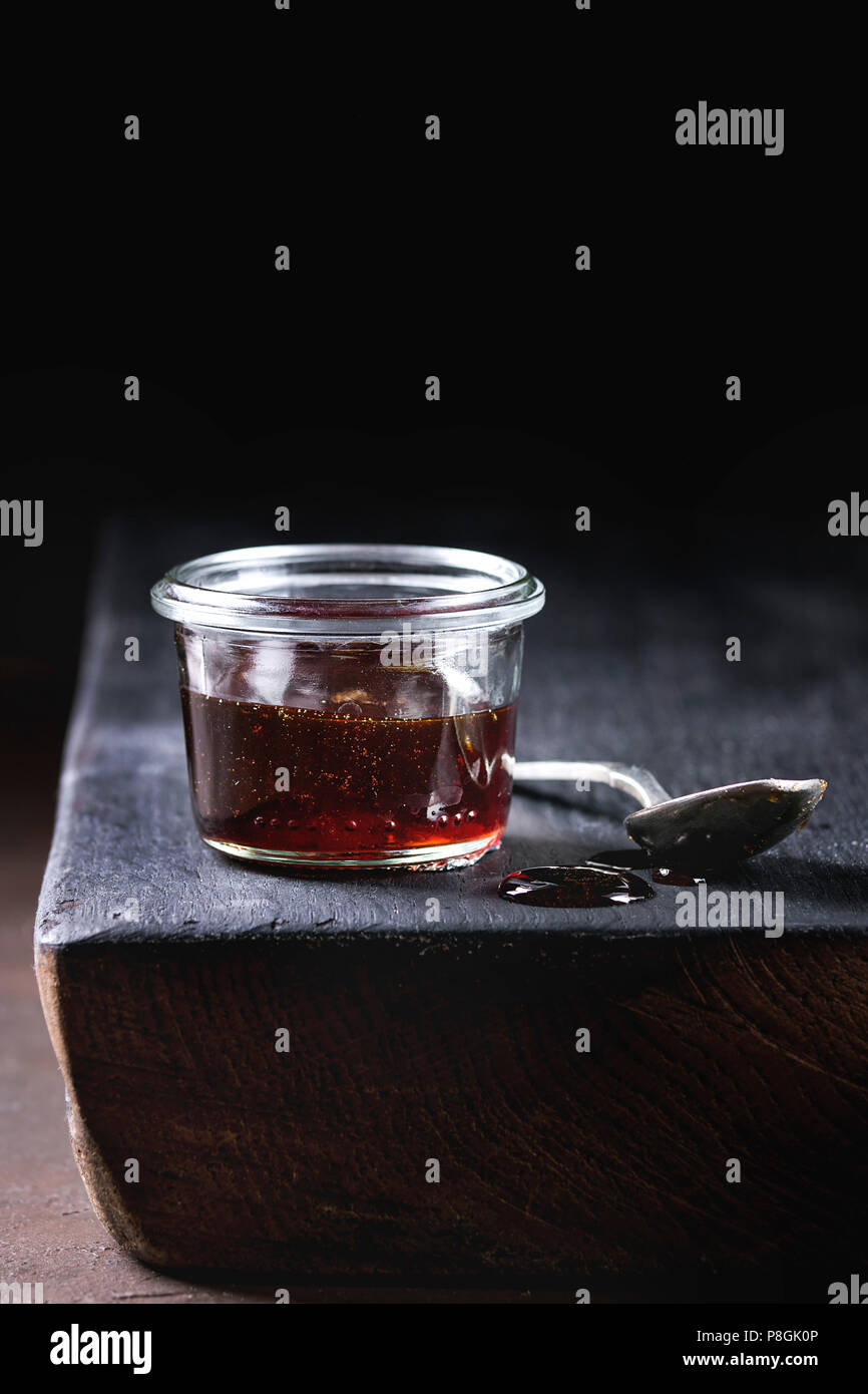 Hausgemachte Flüssigkeit transparent Brown Sugar caramel im Glas steht auf schwarze Holzbrett mit Löffel. Stockfoto