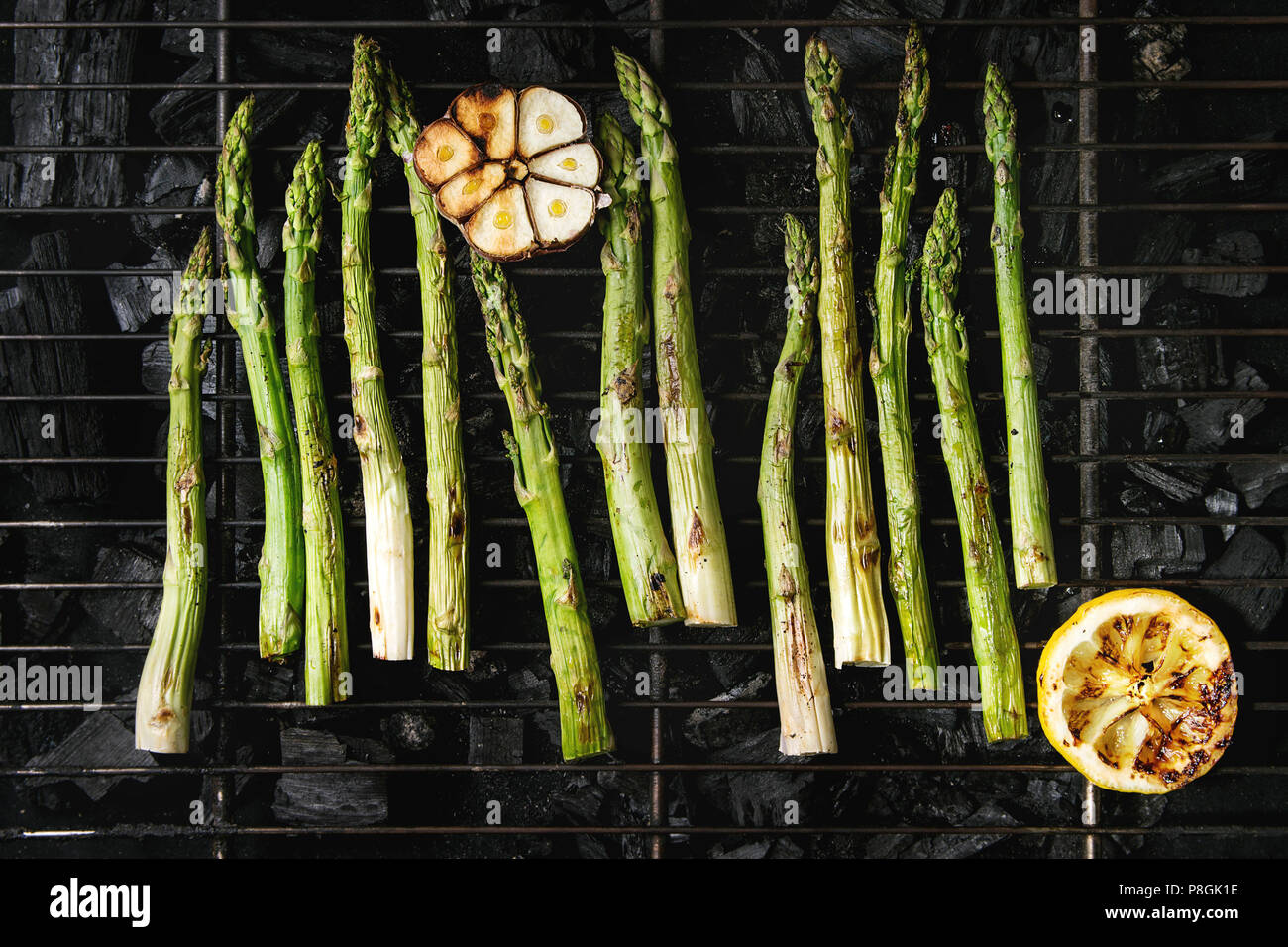 Gegrilltes Gemüse grüner Spargel, Knoblauch, Zitrone auf BBQ Grill Rack über Kohle. Ansicht von oben, Platz. Stockfoto