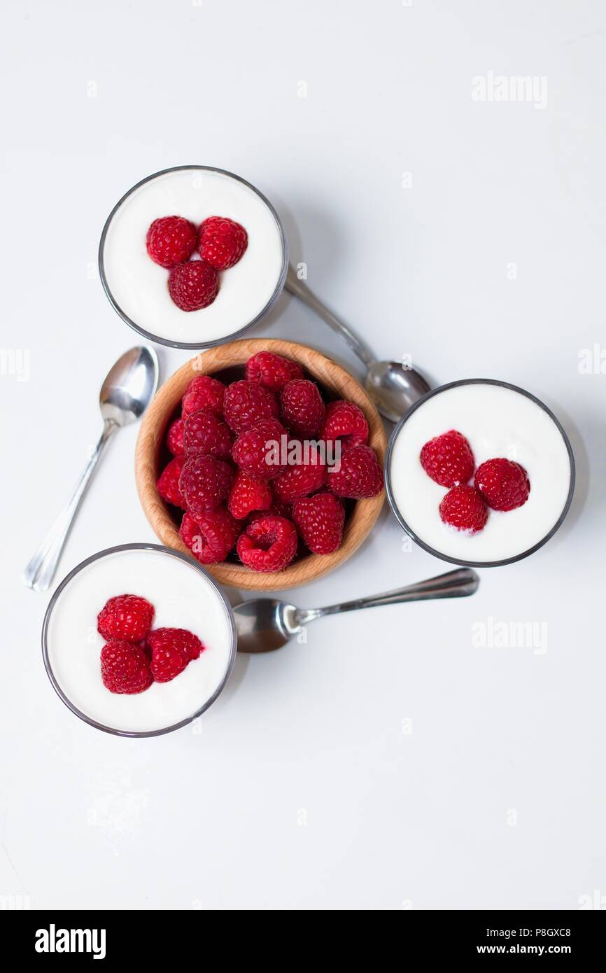 Top down Sicht auf drei Tassen Joghurt mit Löffel um Holz- Schale mit frischen Himbeeren angeordnet Stockfoto