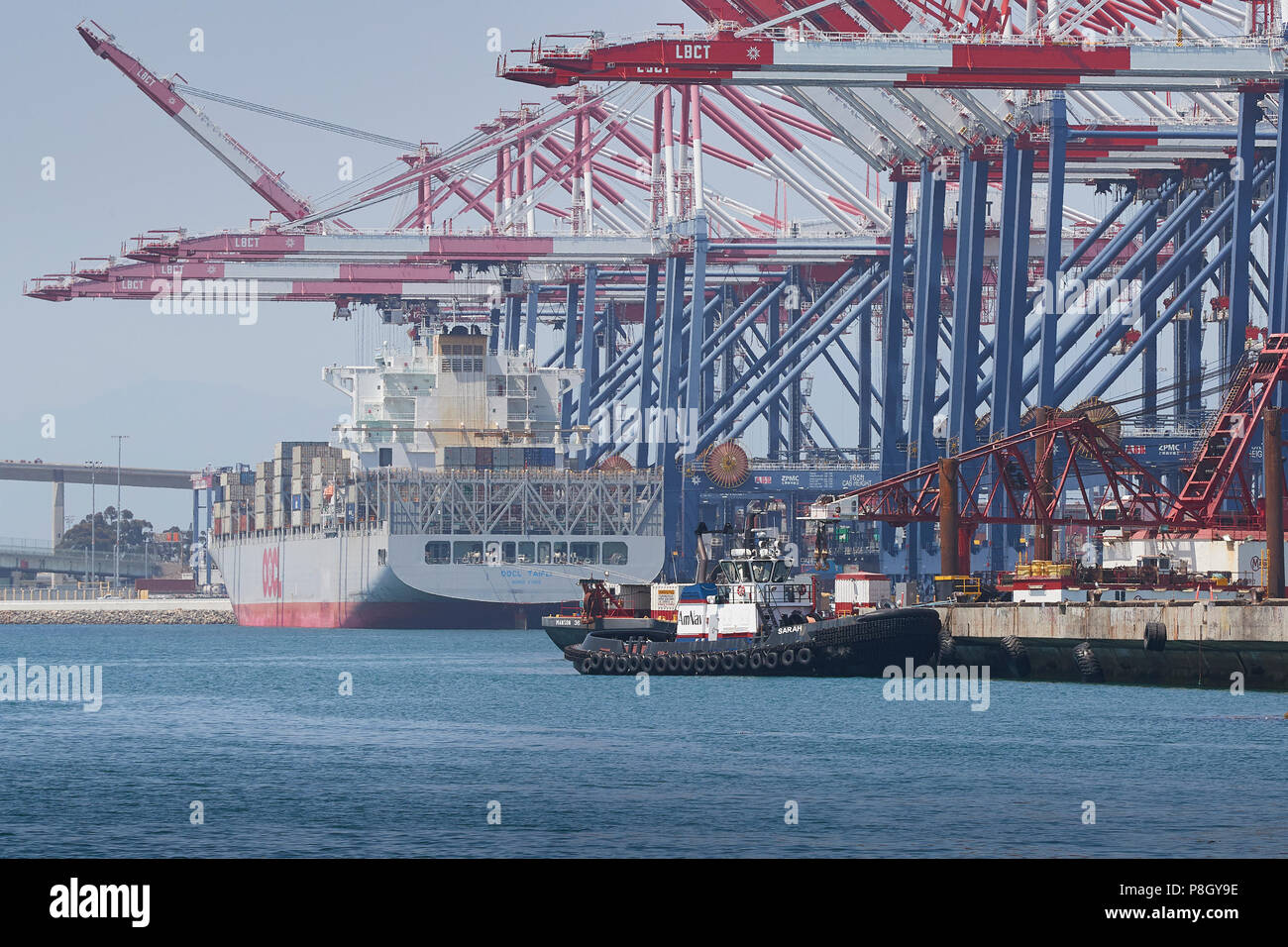 AmNav Tugboat'S ARAH', der in der Lange Strand Container Terminal, die OOCL TAIPAI Container schiff Be- und Entladen Hinter vertäut. Kalifornien, USA. Stockfoto