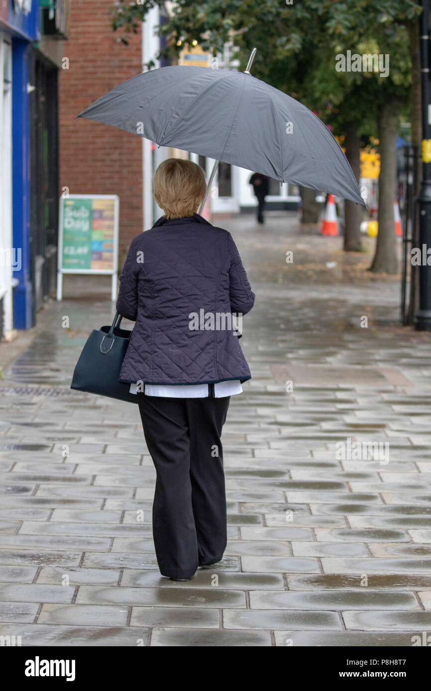 North Wales, 12. Juli 2018, UK Wetter: bewölkt und kühler Start in den Tag für einige mit dem ersten Regen für viele Wochen mit einigen Duschen, schwer und thundery, die Überschwemmungen verursachen können gekoppelt. Frauen wandern im Regen mit Regenschirm in der Marktstadt Form in Flintshire, Wales, UK Credit: DGDImages/Alamy leben Nachrichten Stockfoto