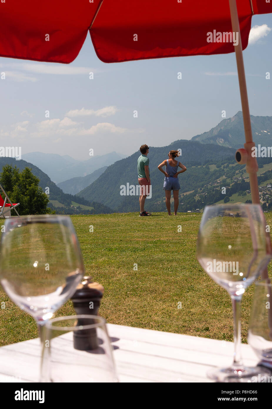 Ein junges Paar sich mit Blick auf die Berge im Garten in Le Chasse-Montagne mit Tabellen mit Weingläsern in Les Gets Frankreich Haute-Savoie Stockfoto