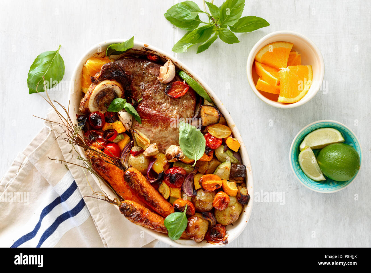 Reisgericht mit Rindfleisch gebacken mit Gemüse (Kartoffeln, Karotten, Aubergine, Zucchini und Tomate) in Keramik Topf auf hölzernen weißen Hintergrund mit Basilikum Sauce Stockfoto