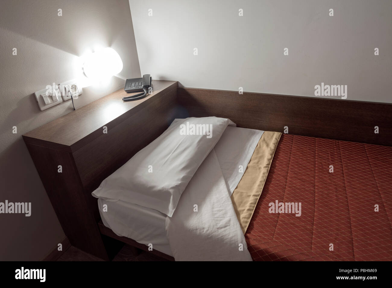 Hotel Bett mit Holzregal, Telefon- und Wandleuchte Stockfoto
