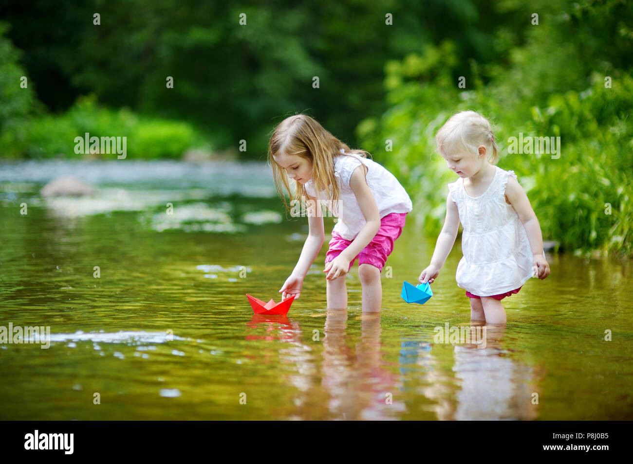 Zwei Entzückende kleine Schwestern spielen mit Papier Boote in einem Fluss Stockfoto