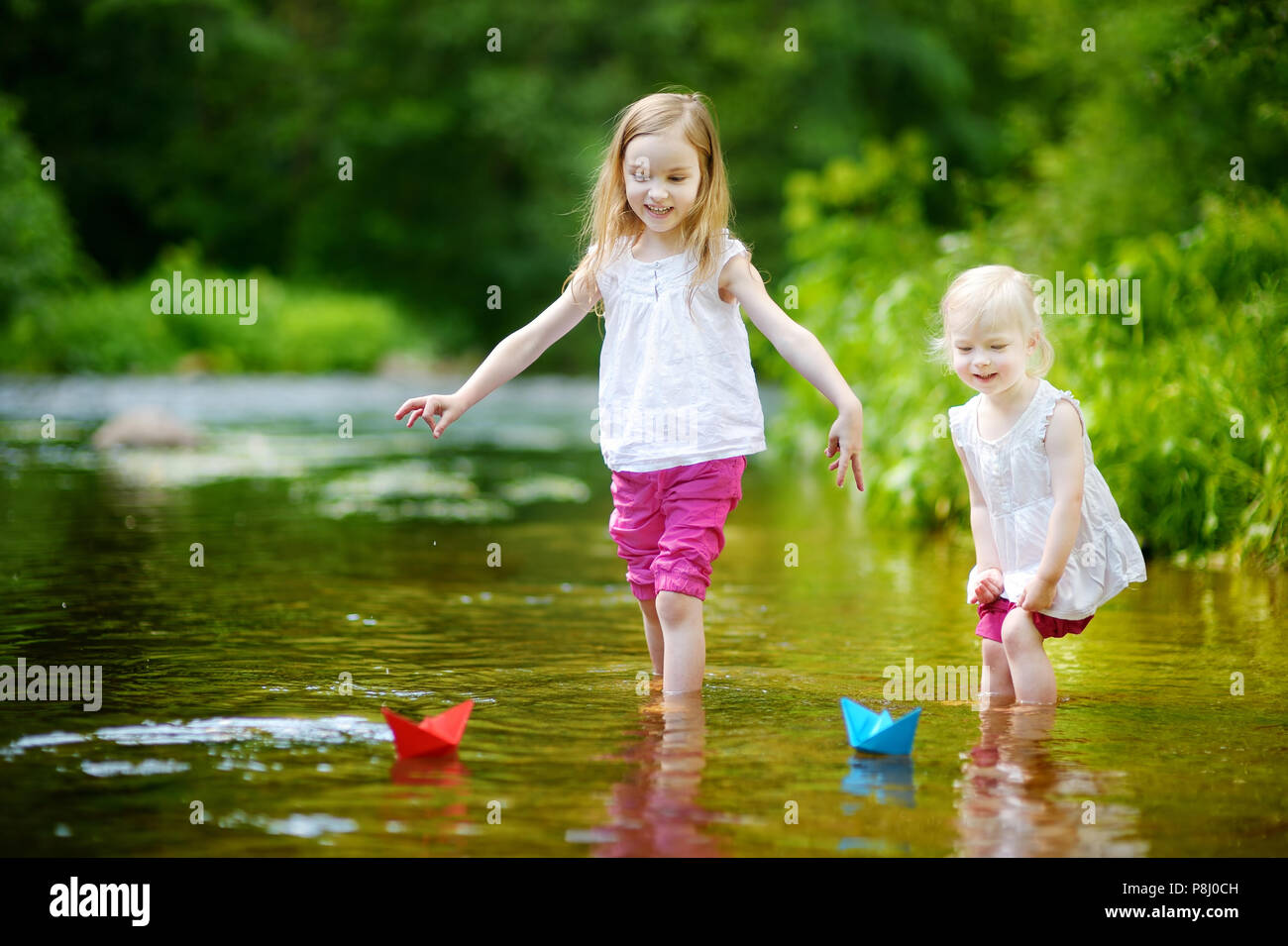 Zwei Entzückende kleine Schwestern spielen mit Papier Boote in einem Fluss Stockfoto