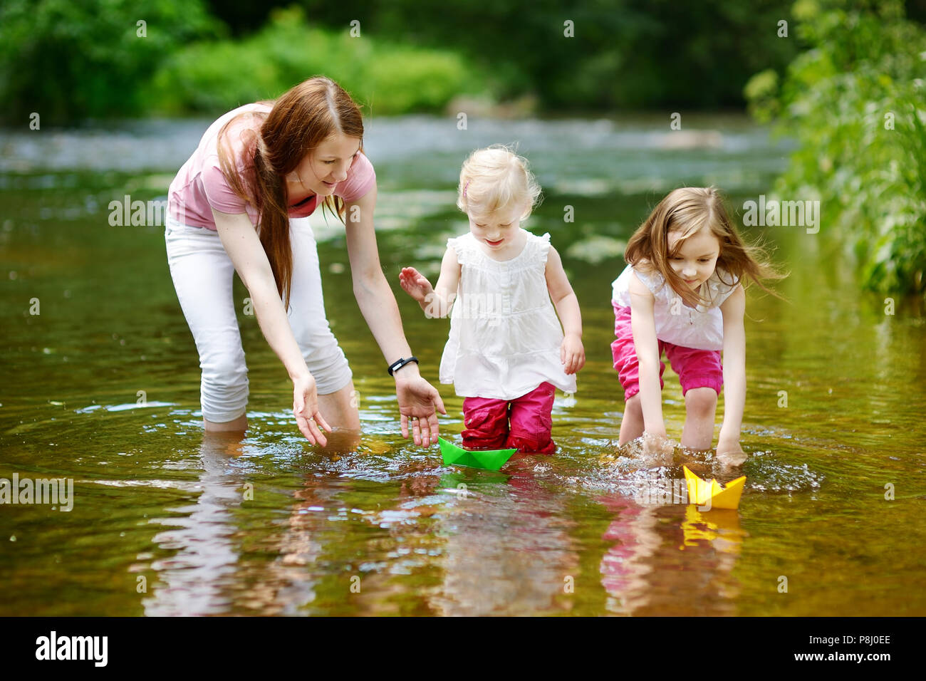 Zwei kleine Schwestern und ihre Mutter spielen mit Papier Boote in einem Fluss Stockfoto