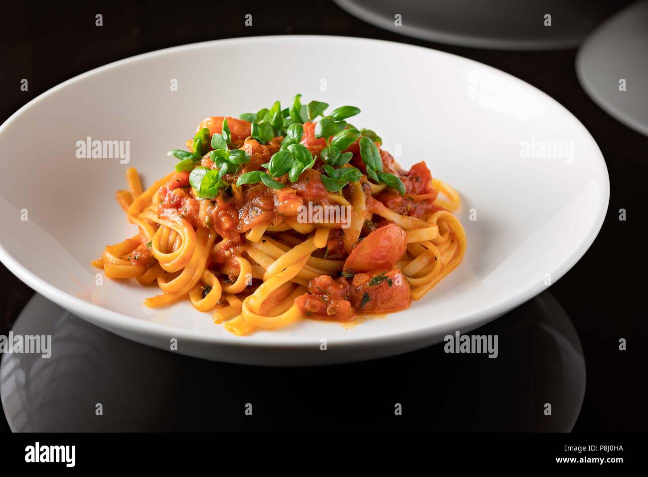 Frische Linguini mit Tomatensauce und Kräutern, serviert auf einem tiefen weißen Teller Stockfoto