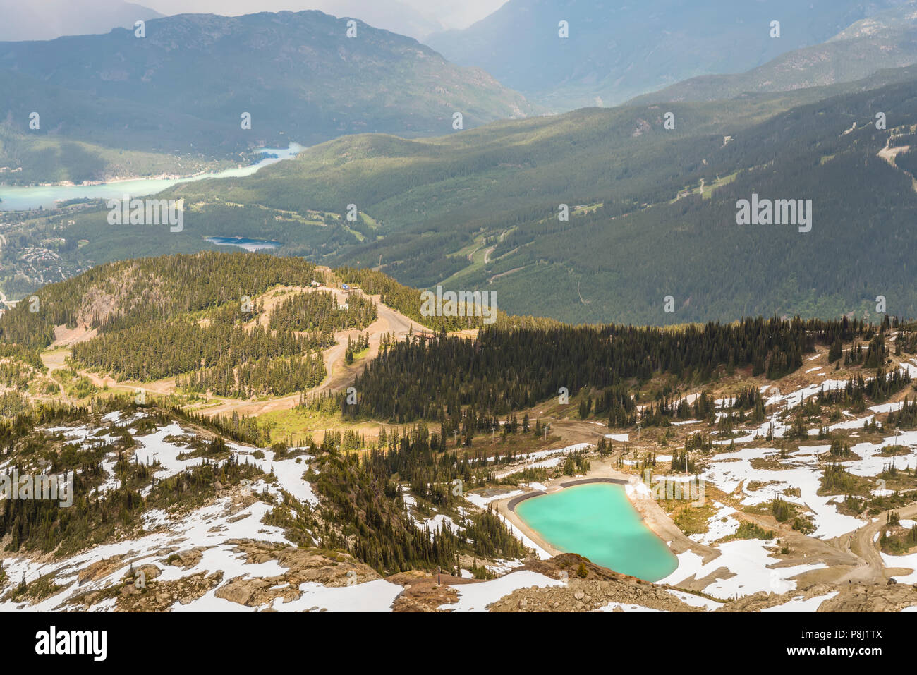 Ein Blick von Oben auf die Berge und Hügel zwischen zwei Seen, von einem dichten Nadelwald und Landstraßen, Schnee auf dem Gipfel des Berges umgeben Stockfoto