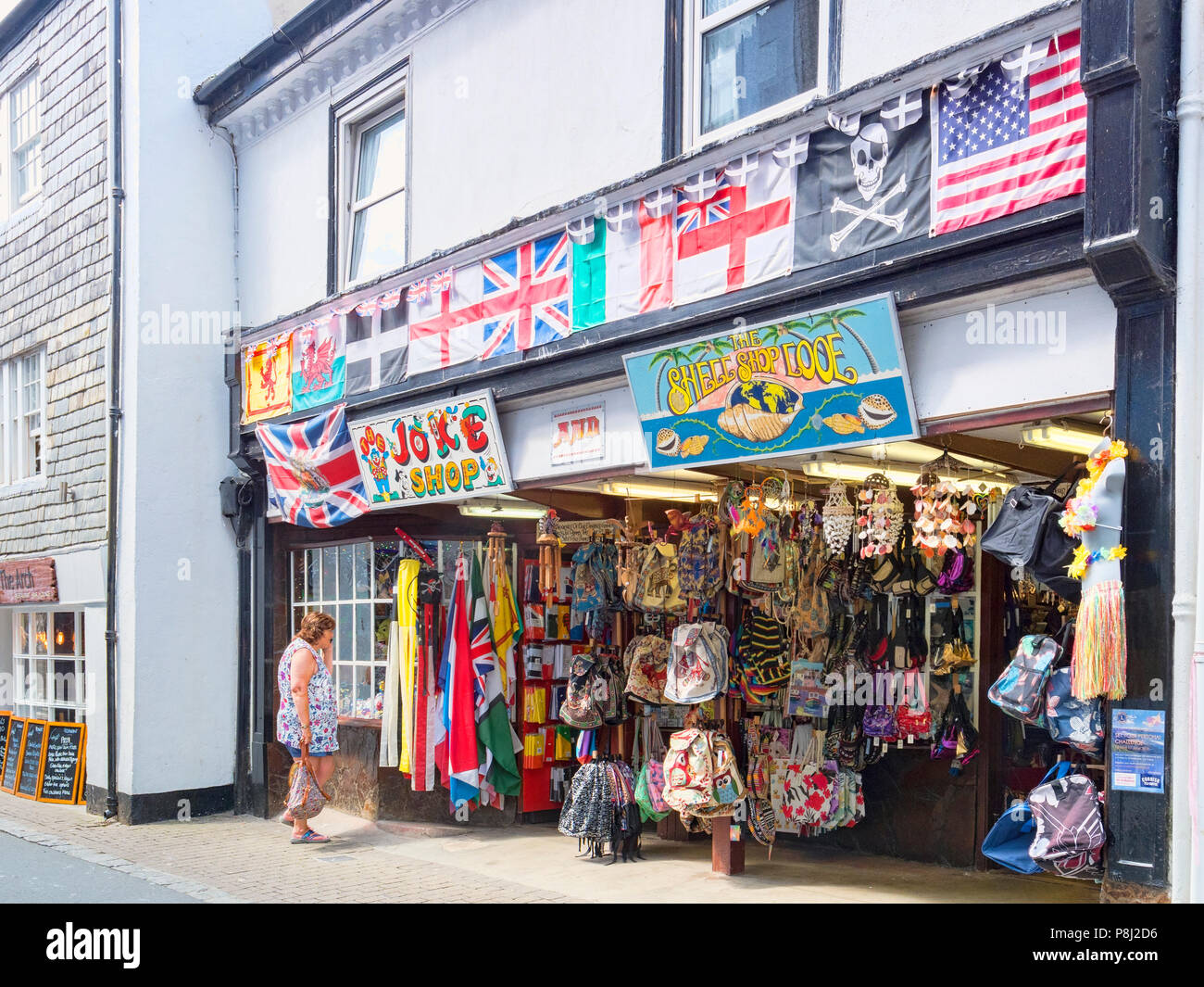 Vom 6. Juni 2018: Looe, Cornwall, UK-Geschäfte im Buller Straße, mit einem Witz Shop und eine Shell Shop. Frau Suchen in Fenster. Stockfoto
