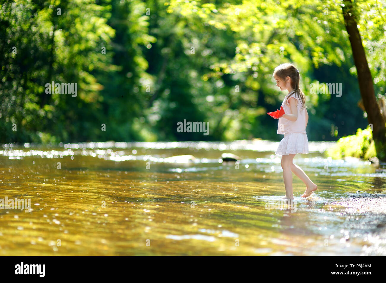 Adorable kleine Mädchen spielen mit Papier Boote durch einen Fluss an warmen und sonnigen Sommer Tag Stockfoto