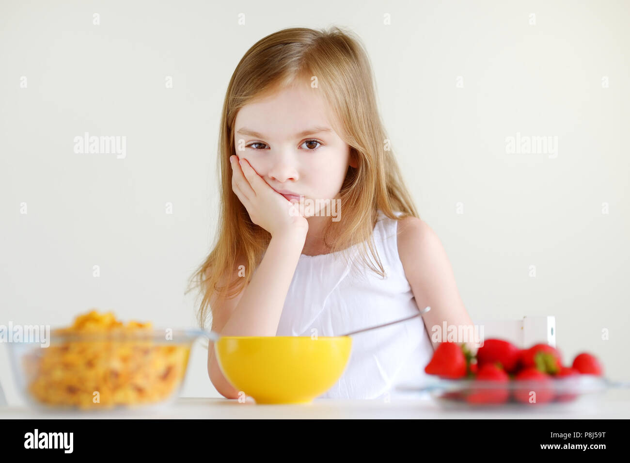 Adorable kleine Mädchen mit Müsli mit Erdbeeren in weißer Küche Stockfoto