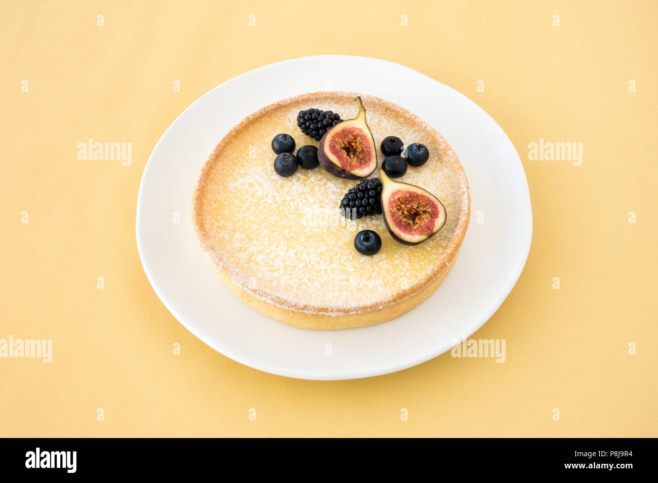 Lemon tart in Scheiben geschnitten und mit frischen Feigen, Heidelbeeren und Brombeeren auf hellgrauem Hintergrund mit Kopie Raum eingerichtet. Ansicht von oben. Stockfoto