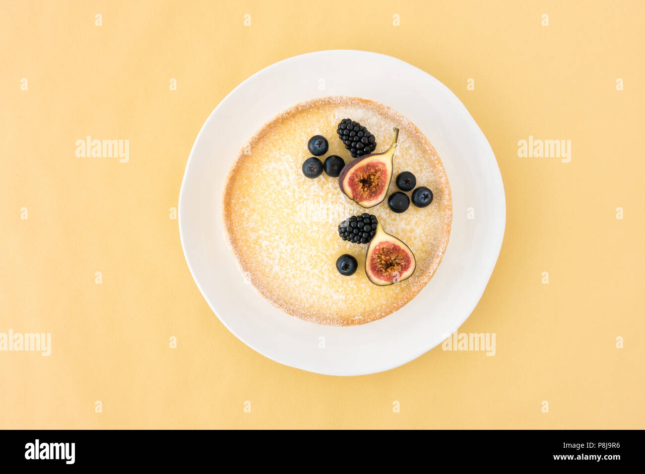 Ansicht von oben in eine Zitrone Törtchen mit frischen Feigen, Heidelbeeren und Brombeeren auf gelbem Hintergrund mit Kopie Raum eingerichtet. Stockfoto