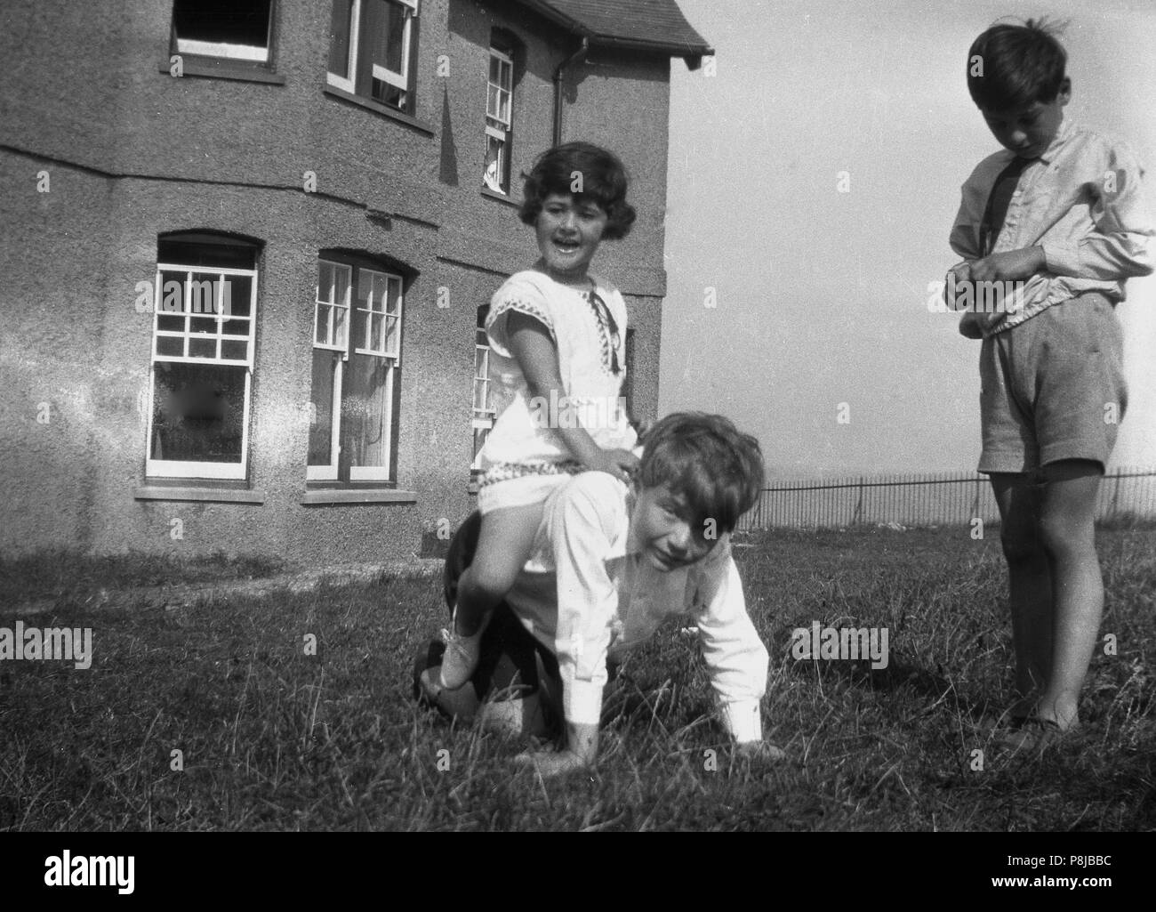 1950er Jahre, junge Kinder spielen im Freien ein Haus auf Gras, ein junges Mädchen - vorgibt, sie ist ein Pferd reiten - sitzen auf einem Jungen, der auf seinen Händen und Knien, England, UK. Stockfoto