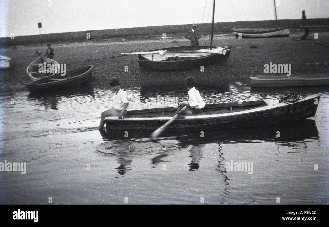 1930er Jahre, historische, zwei Jungen in einem hölzernen Ruderboot in einer ruhigen Einlass von Wasser, einer Dong das Rudern, die anderen sitzen auf der Rückseite, England, UK. Stockfoto