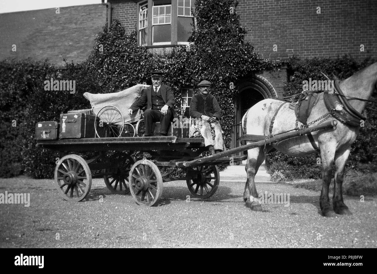 1930er Jahre, historische Bild, auf der Zufahrt außerhalb ein großes Haus zwei männlichen Bediensteten auf dem Rücken der Pferde und Wagen mit Gepäck Stämme der Epoche und einer überdachten Kinderwagen, England, Großbritannien geladen. Stockfoto