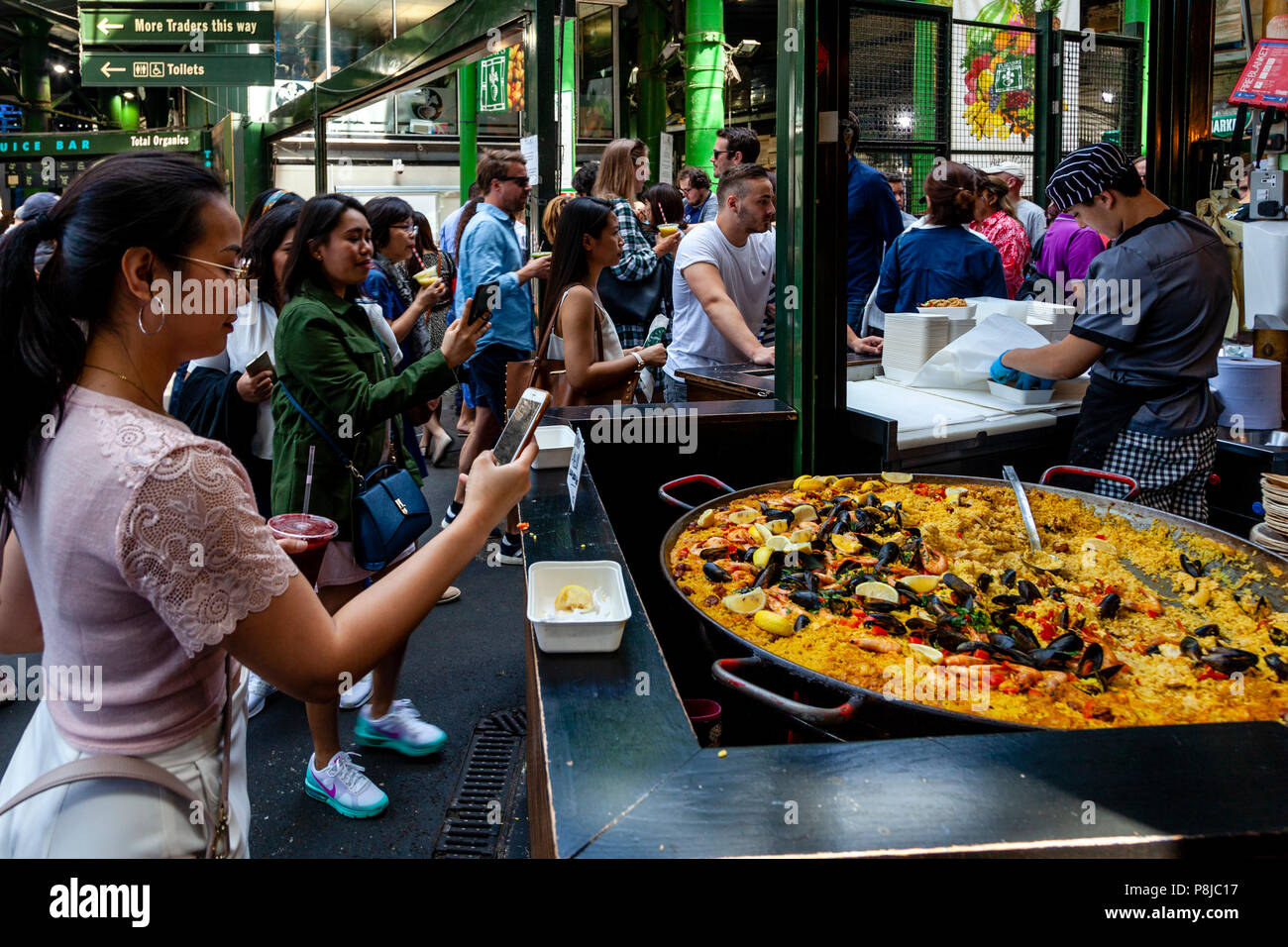 Asiatische Touristen Fotos von einem grossen Teller von Takeaway Paella am Borough Market, London, England Stockfoto