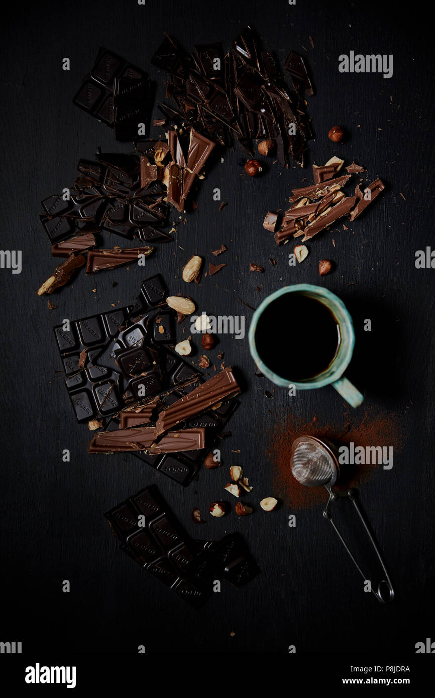 Zerkleinerte Schokolade auf schwarzem Hintergrund mit Kakao Pulver, Nüsse und Kaffee. Schwarzer Hintergrund, Ansicht von oben Stockfoto