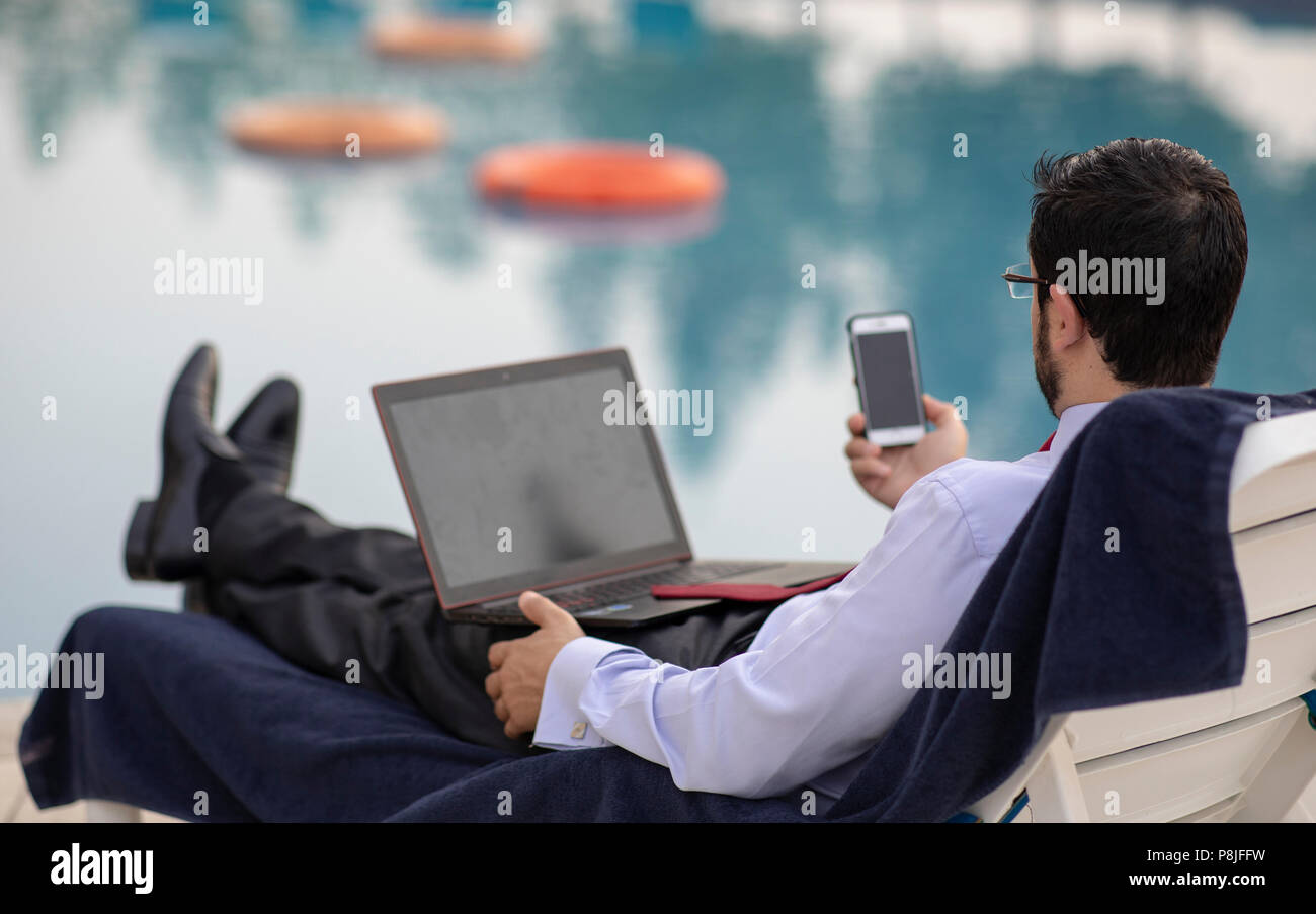 Im mittleren Alter arabischer Mann arbeiten während seinen Sommerurlaub durch einen Pool Stockfoto