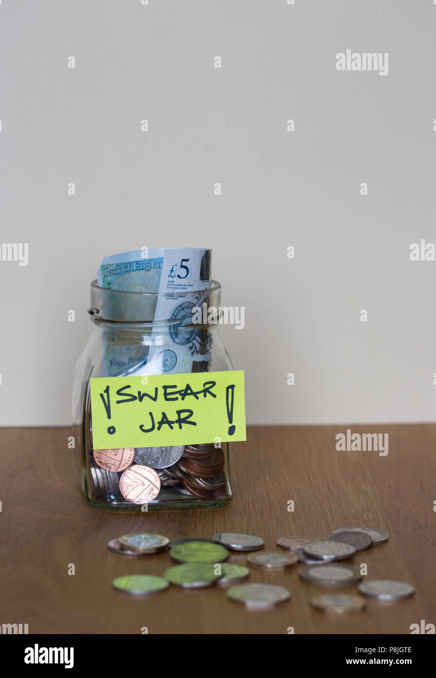 Glas schwören jar mit einem gelben Etikett auf einem Holztisch mit zusätzlichen Münzen auf den Tisch Stockfoto