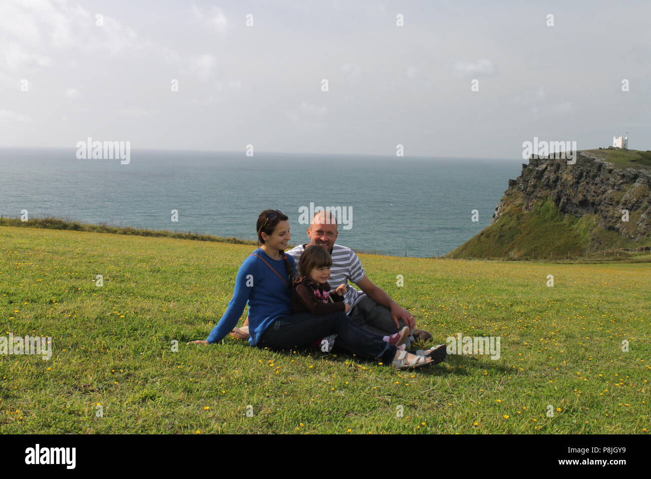 Vater schönen Mutter und Tochter Familie kuscheln mit dem Meer im Hintergrund in Cornwall. Stockfoto