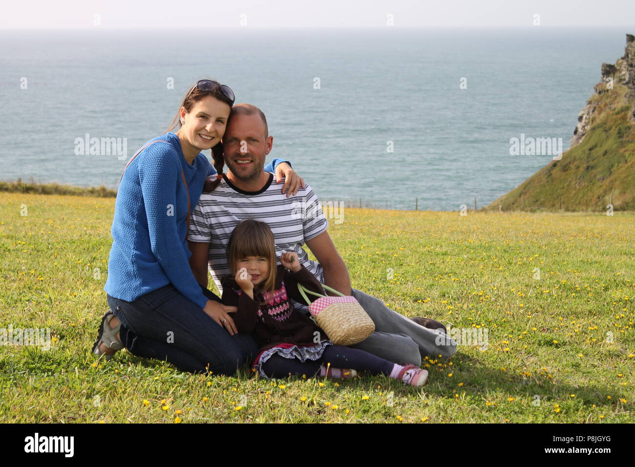 Vater schönen Mutter und Tochter Familie kuscheln mit dem Meer im Hintergrund in Cornwall. Stockfoto