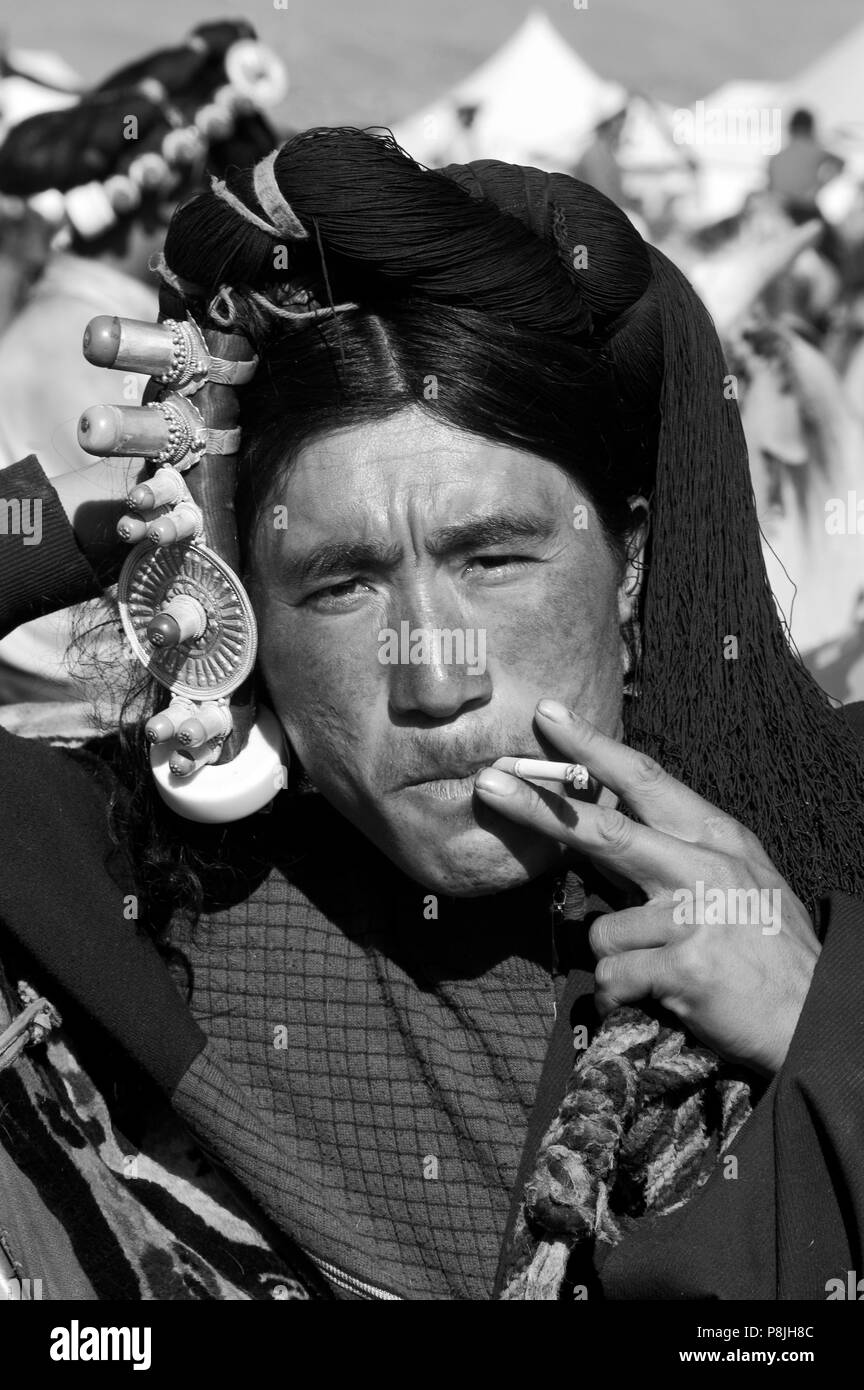 Khampa Mann mit Gold & coral Haar peices raucht am Litang Horse Festival, Kham, Provinz Sichuan, China (Tibet) Stockfoto
