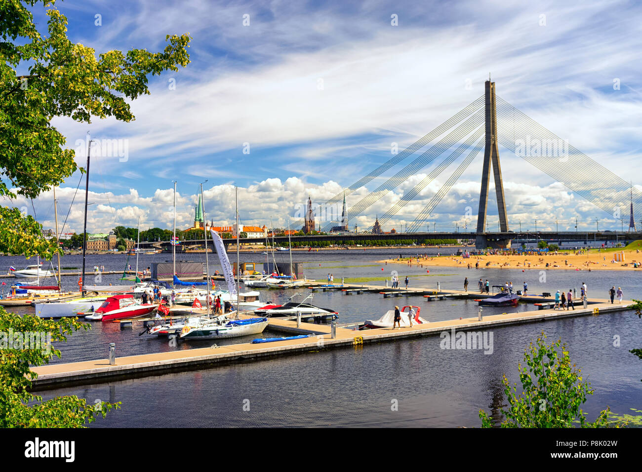 Weiße Yachten mit hohen Masten vor dem Panorama der Stadt Riga mit spiers der Kathedralen und einer Schrägseilbrücke über den Fluss Daugava auf Stockfoto