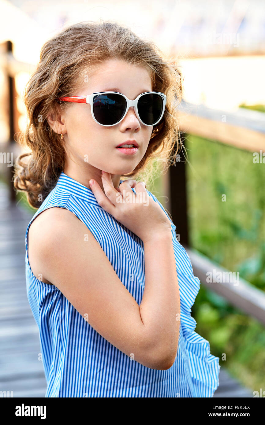 Elegante Kind Portrait. Kleines Mädchen Modell tragen Sommer kühl Kleidung, Sonnenbrillen. Marine Stil, im Freien. Weg schauen. Fashion kid Konzept. Stockfoto