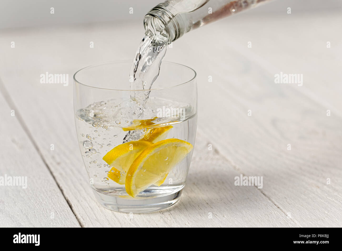 Das Gießen von Wasser aus einer Flasche in ein Glas mit Zitronenscheiben. Weiß Holz Hintergrund. Stockfoto