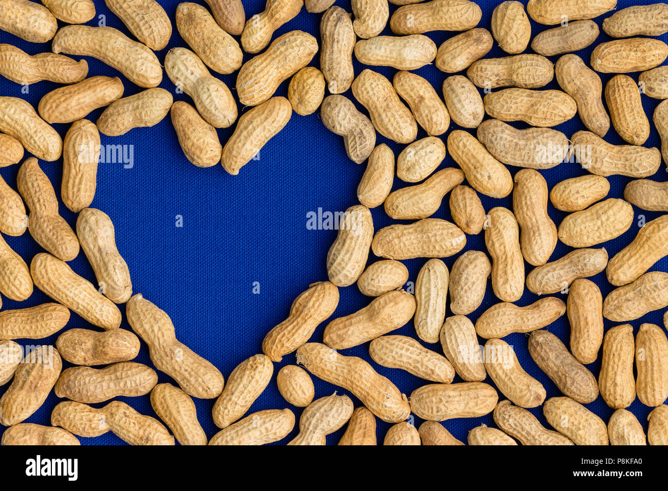 Rahmen mit einer ordentlichen Schicht von natürlichen Ganzen gesunden Erdnüsse oder Erdnüsse in ihren Hülsen oder Muscheln rund um ein blaues Herz Form mit Kopie der Platz in einem conceptu Stockfoto