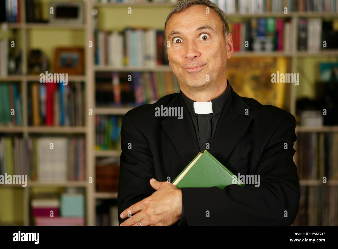 Ein katholischer Priester ist das Studium in seine Bibliothek. Er schaut uns mit Verrücktheit, Zinsen, Ablehnung, Urteil und Besorgnis. Stockfoto