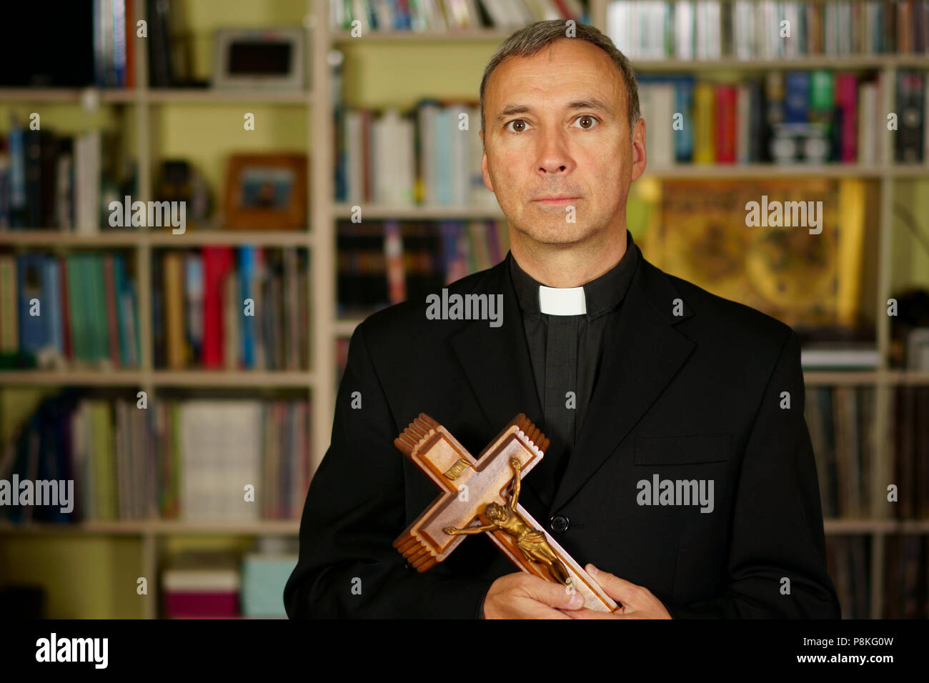 Eine gut aussehende ernsthafte katholische Priester zeigt ein Kruzifix. Er schaut ernst zu nehmen, uns mit Interesse, Nachdenklichkeit und Missionierung. Stockfoto