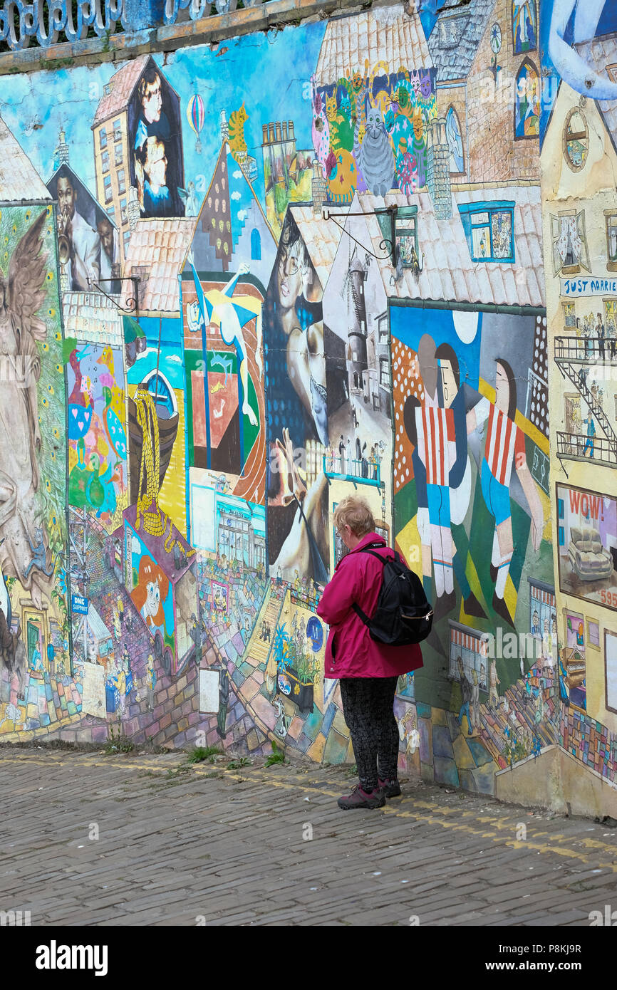 Ältere Menschen, Rentner lady Phone gegen Streetart, Graffiti Wand auf gepflasterten Straße von blands Klippe, Yorkshire Ferienort Scarborough, Großbritannien Stockfoto