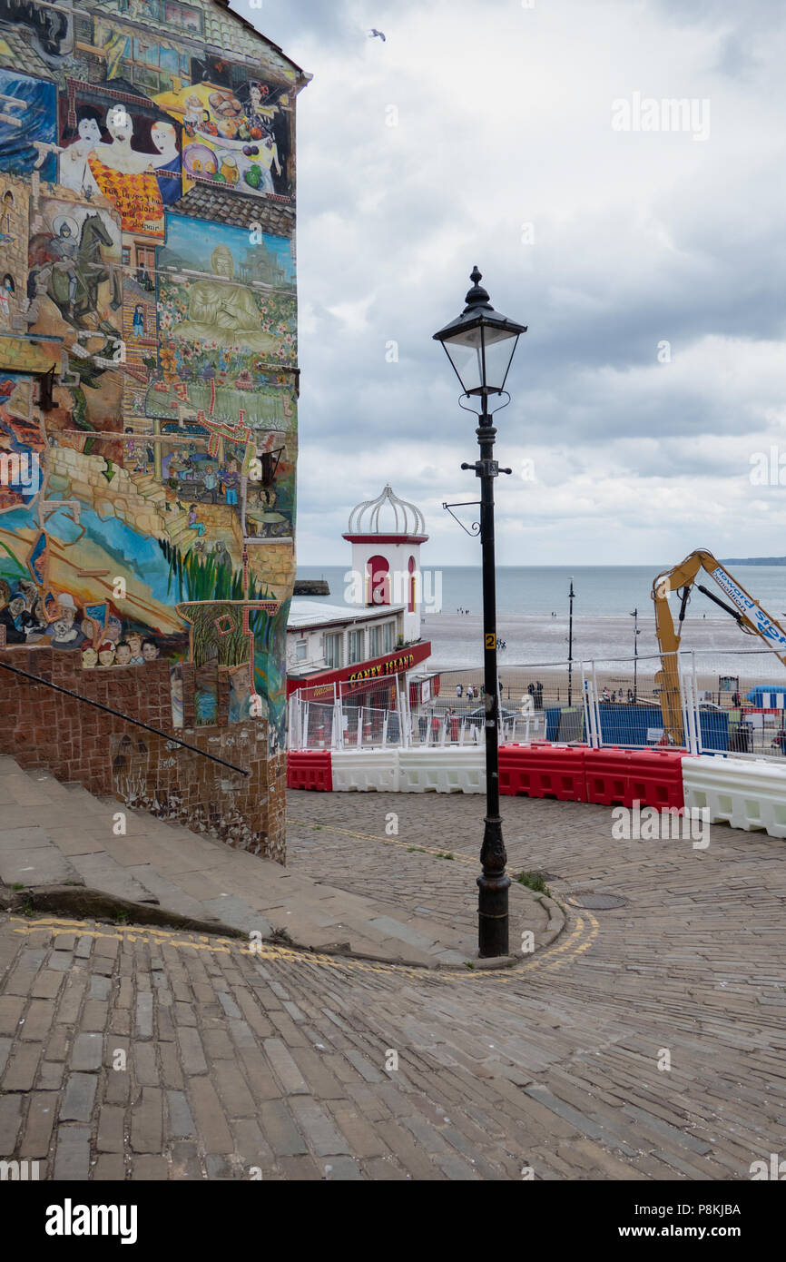 Alte Strassenlaterne und Gebäude mit street art auf der Seite mit Blick auf das Meer mit neuen Gebäude nur in Bild bei Scarborough, North Yorkshire, Großbritannien gebaut Stockfoto