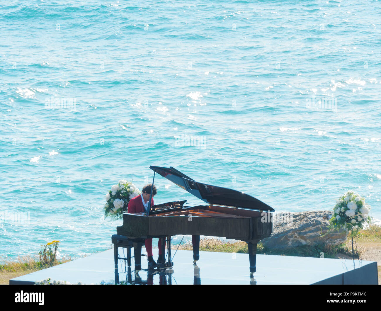 Newquay, Cornwall, England. 12. Juli 2018. Rosamunde Pilcher Schauspieler Manuel Mairhoffer spielt Klavier auf den Klippen, Filmen 'Meine Brüder Braut' Fistral Beach, UK, 12., Juli, 2018 Robert Taylor/Alamy Leben Nachrichten. Newquay, Cornwall, England. Credit: Robert Taylor/Alamy leben Nachrichten Stockfoto