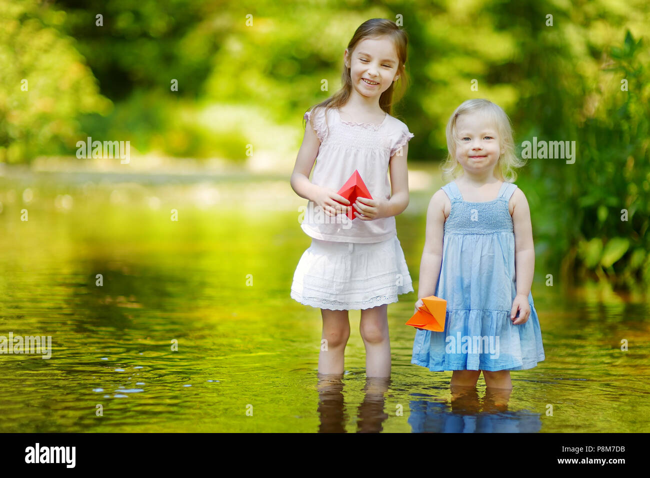 Zwei kleine Schwestern spielen mit Papier Boote durch einen Fluss an warmen und sonnigen Sommer Tag Stockfoto