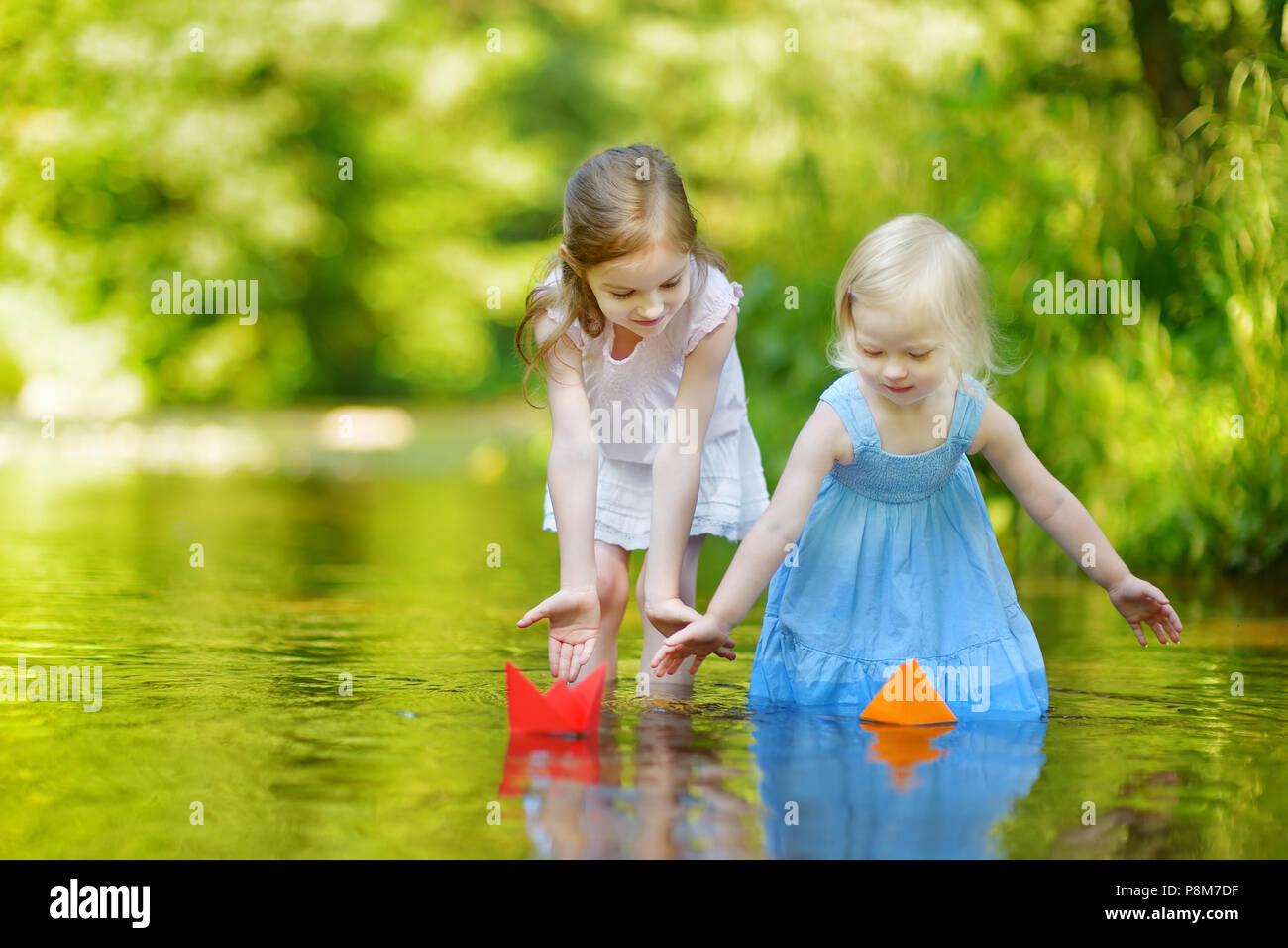 Zwei kleine Schwestern spielen mit Papier Boote durch einen Fluss an warmen und sonnigen Sommer Tag Stockfoto