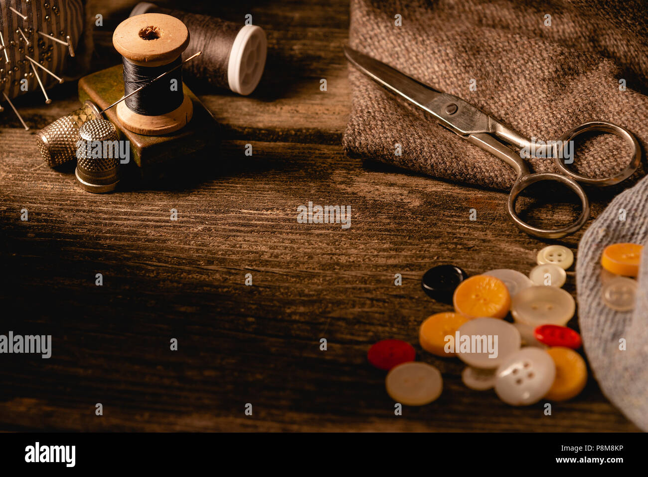 Nahaufnahme des Nähens Spulen mit weißen und schwarzen Faden und Nadel, Fingerhüte und die Vielfalt der bunten Tasten auf Holzbrett Tabelle einstellen Stockfoto