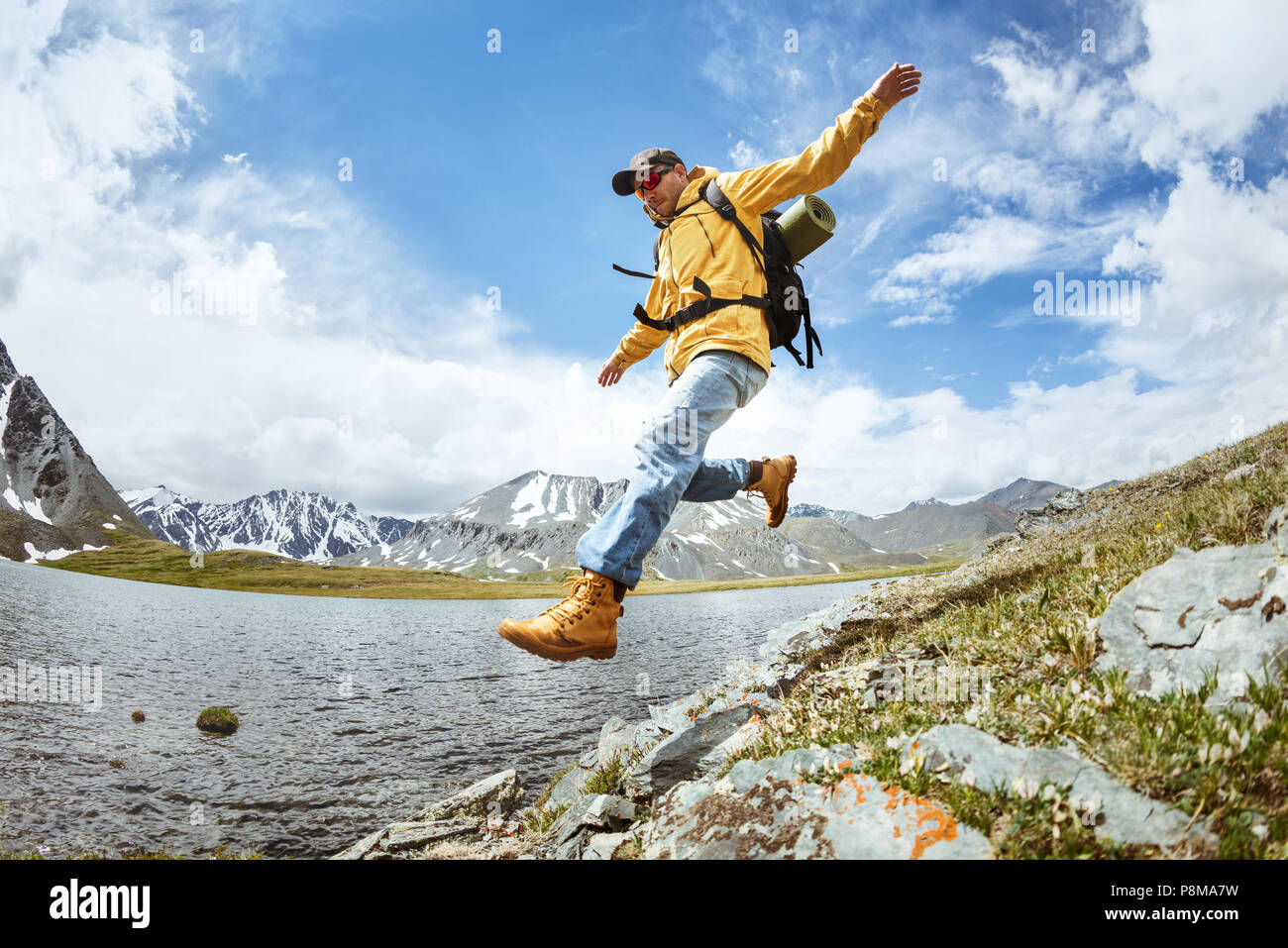 Mann Wanderer springt von großen Felsen im Gebirge gegen See Stockfoto