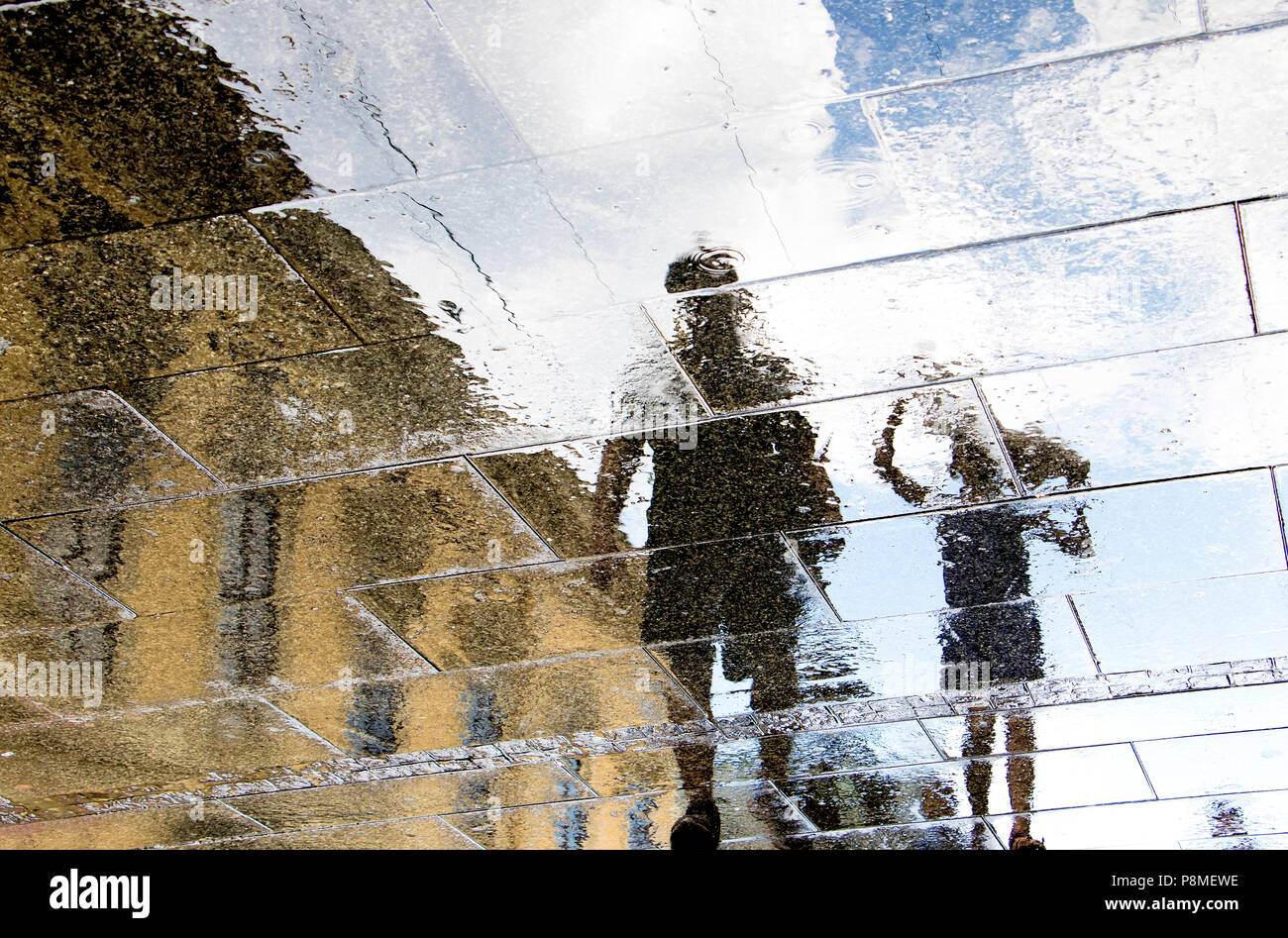 Unscharfe Reflexion Schatten Silhouetten von Vater und Kind zu Fuß an einem regnerischen gemusterten Stadt bürgersteig an einem regnerischen Frühlingstag Stockfoto