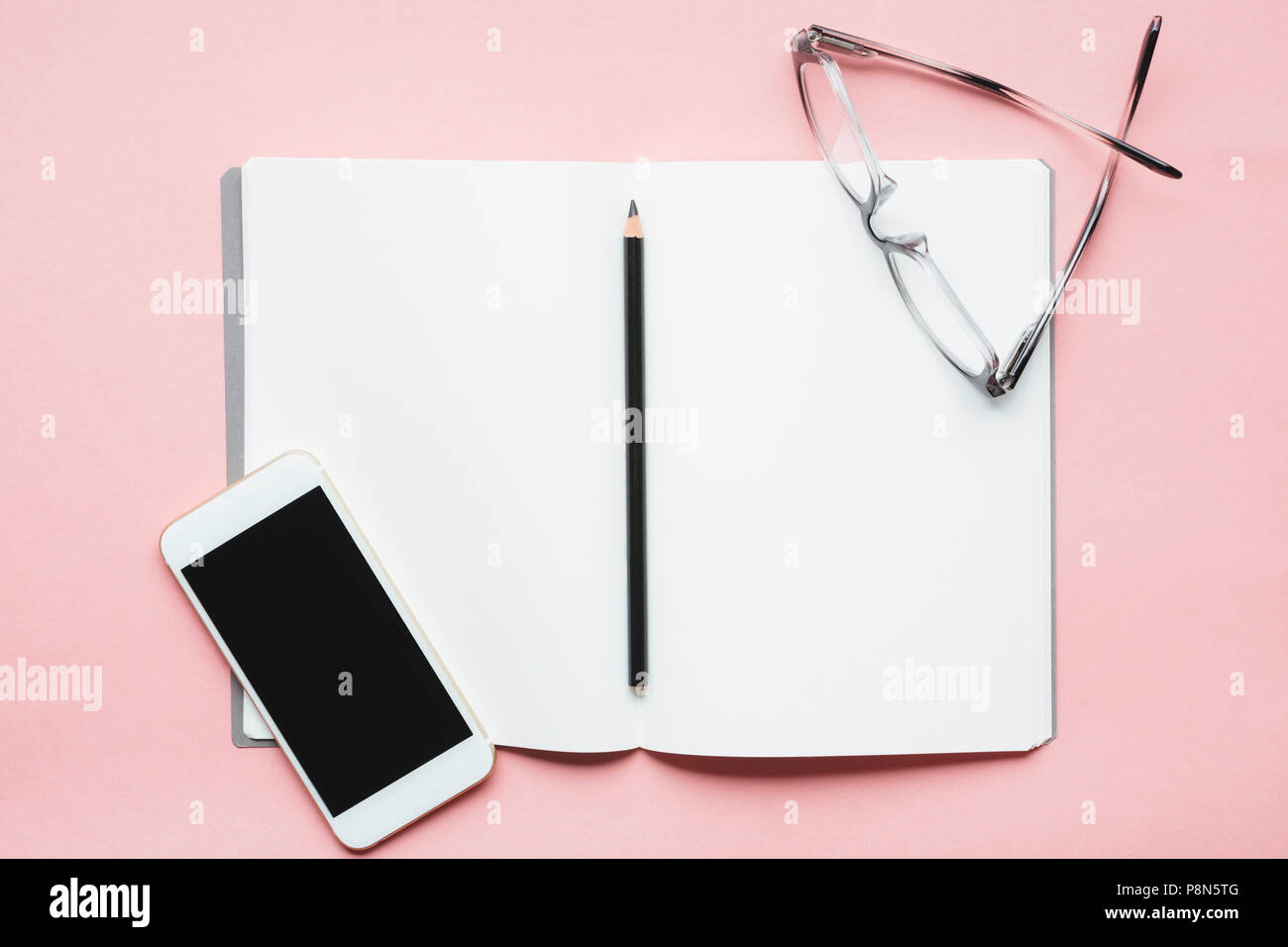 Smartphone, Bleistift und Brille auf offenem Notebook Stockfoto